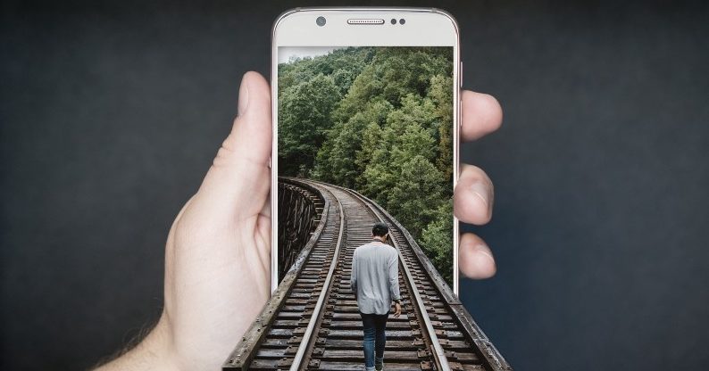 Man wlaking on traintrack on a photo displayed on iPhone (The image come out of the phone)