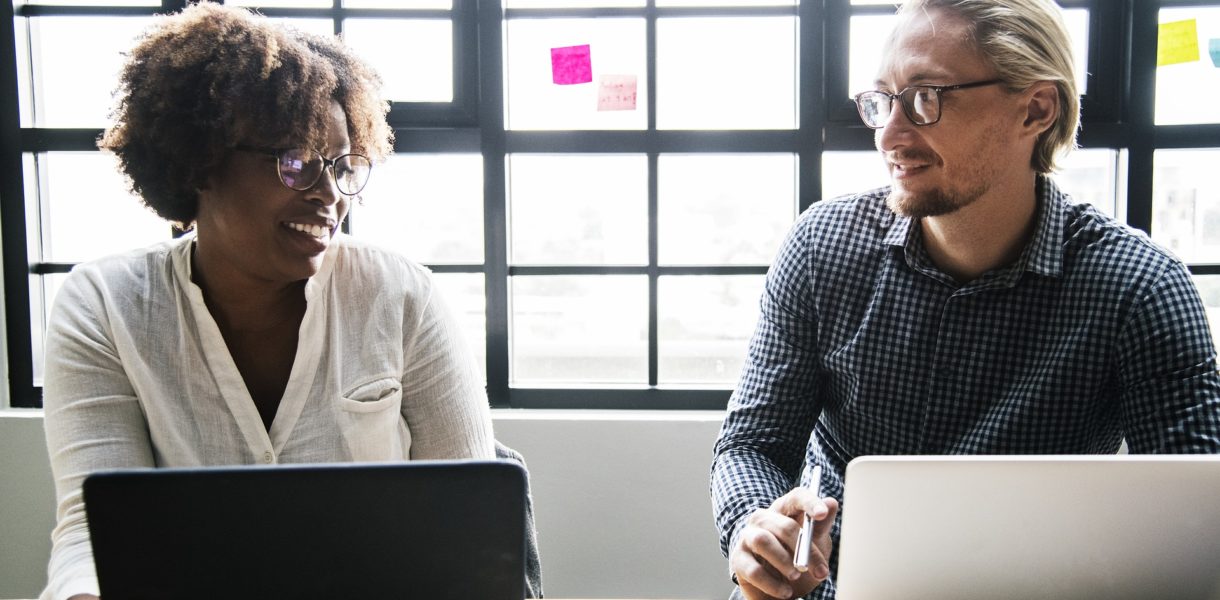 Two people using laptops whilst socialising in a work environment