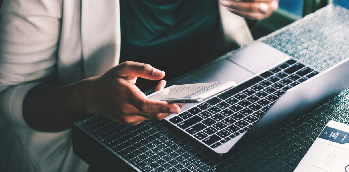 women sitting with computer while typing on phone