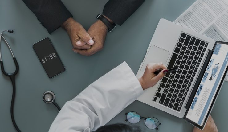 A doctor writing notes on a laptop with a stethoscope on the table