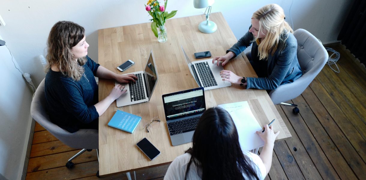 three women sitting at desk with computers