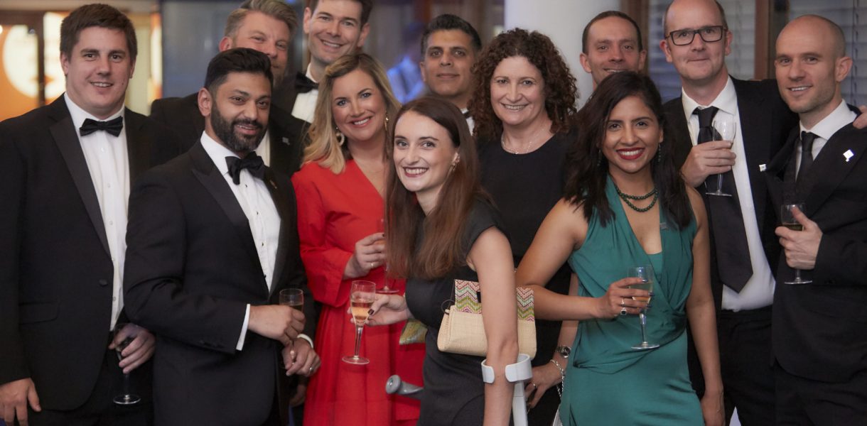 Attendees of the DL100 Awards event gathered around in black tie, smiling at the camera
