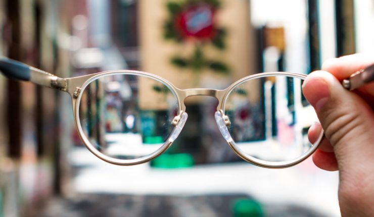 pair of glasses held in front of person on the street