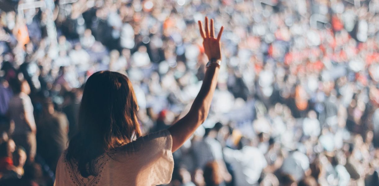woman standing up in crowd, raising her hand