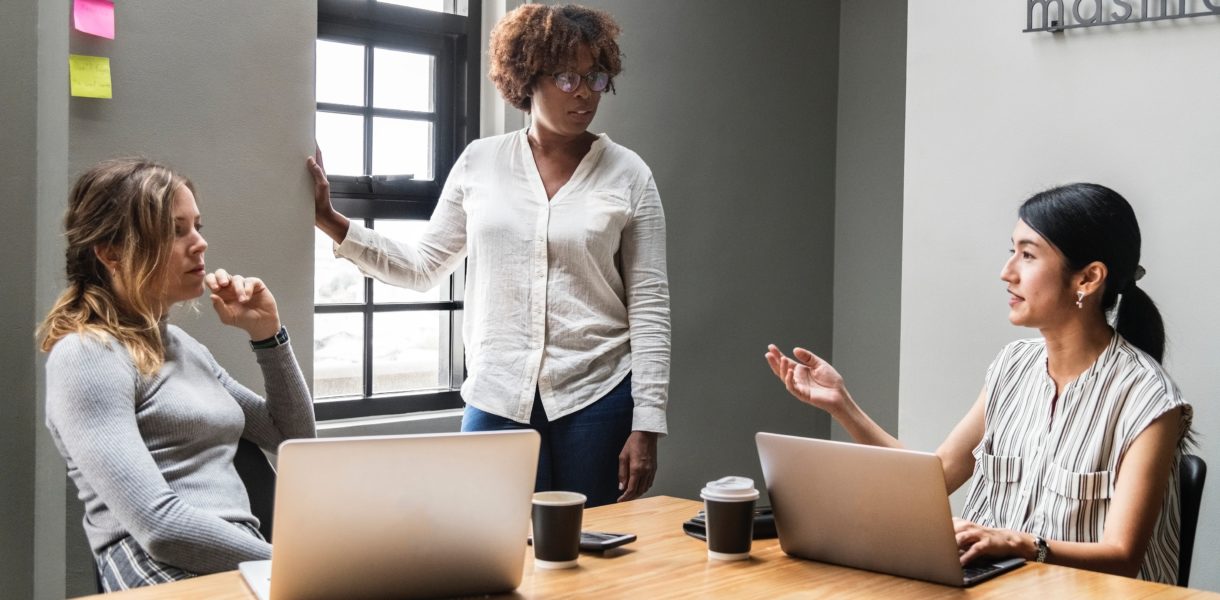 3 women using laptops around a table in a business meeting