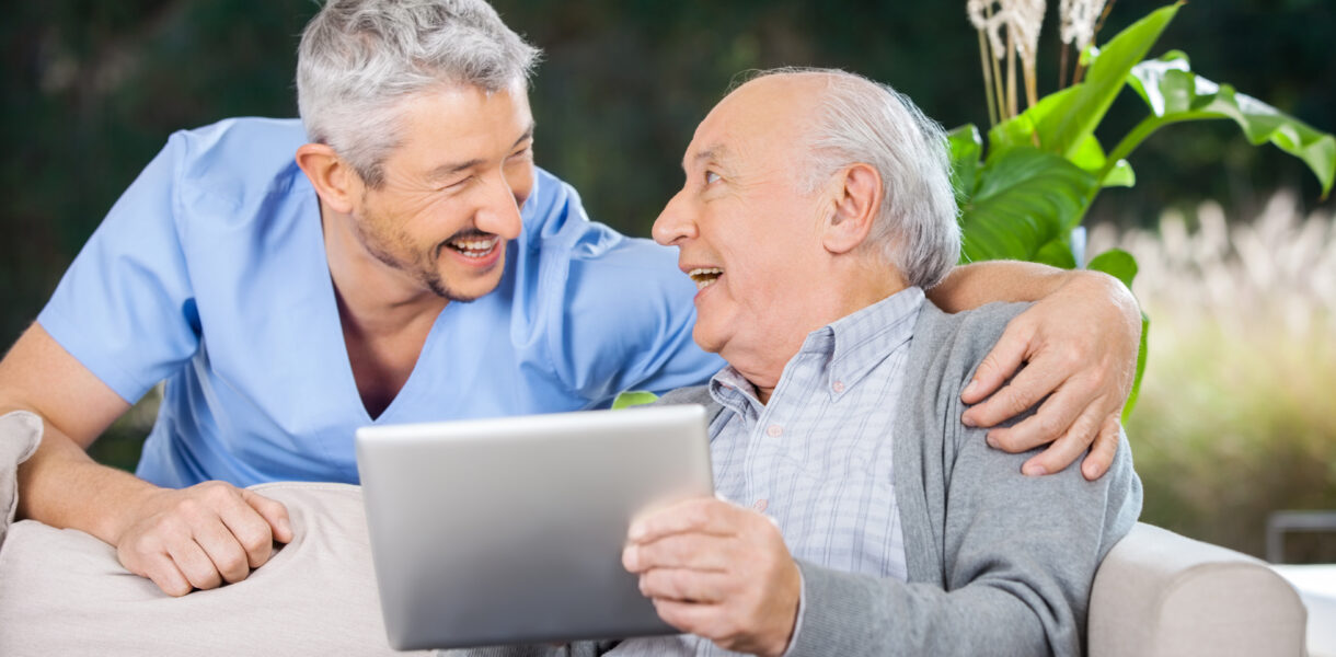 Laughing,Male,Caretaker,And,Senior,Man,Using,Tablet,Computer,At