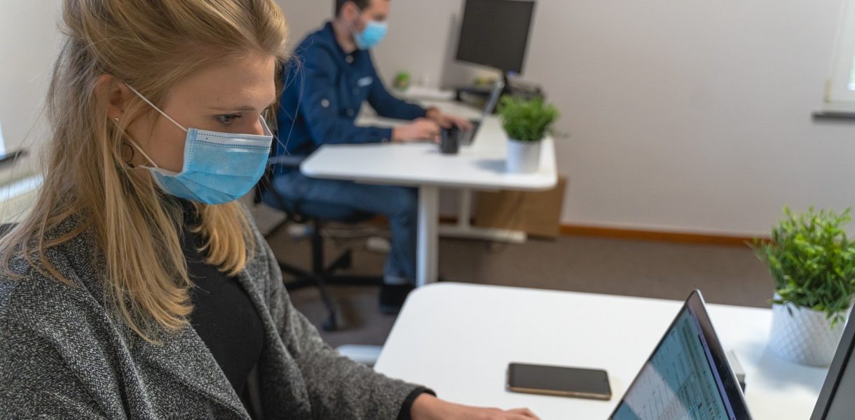 Man and woman in mask using laptops