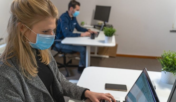 Man and woman in mask using laptops