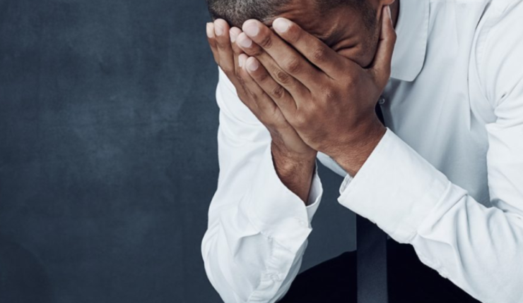Man bend over holding his face in his hands